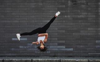 haciendo parkour loco y acrobacias atléticas. joven morena deportiva con forma de cuerpo delgado contra la pared de ladrillo en la ciudad durante el día foto