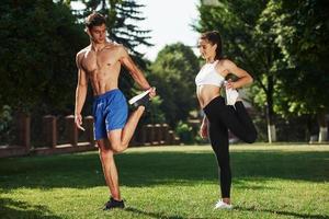 Exercises for legs. Man and woman have fitness day in the city at daytime in the park photo