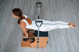 Aerial view. Confident young sporty woman with slim body type in the healthy center doing exercises by using special equipment photo