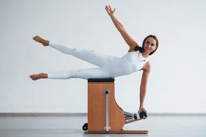 Leaning on the side. Confident young sporty woman with slim body type in the healthy center doing exercises by using special equipment photo