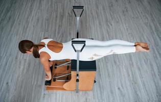 Aerial view. Confident young sporty woman with slim body type in the healthy center doing exercises by using special equipment photo