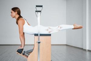 Side view. Confident young sporty woman with slim body type in the healthy center doing exercises by using special equipment photo