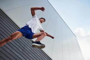 Into the air. Young sports man doing parkour in the city at sunny daytime photo
