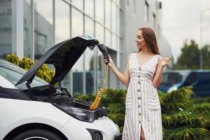 preguntándose acerca de la nueva tecnología. mujer en la estación de carga de coches eléctricos durante el día. vehículo nuevo foto