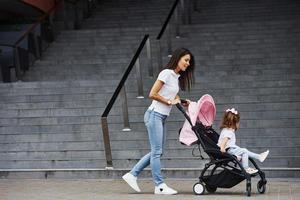 Pretty young mother and her little daughter in pink pram have walk in the city photo