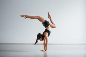 Doing hand stand. Young sporty woman in black clothes with slim body type in the healthy center doing exercises photo