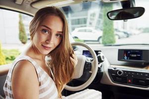 Looks back. Female driver inside of modern automobile. Testing brand new car photo