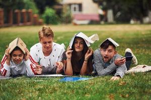 Bored and having fun. Group of young students in casual clothes on green grass at daytime photo