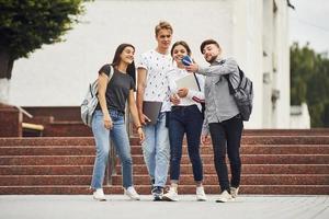 hablando selfie mientras paseaba. grupo de jóvenes estudiantes con ropa informal cerca de la universidad durante el día foto