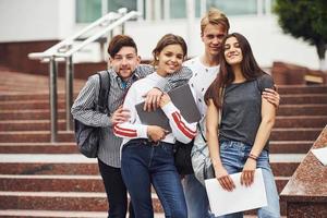 Embracing each other. Group of young students in casual clothes near university at daytime photo