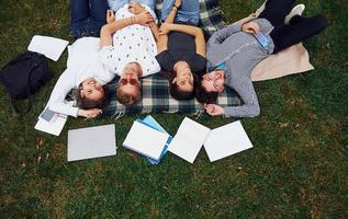 Having good rest. Group of young students in casual clothes on green grass at daytime photo