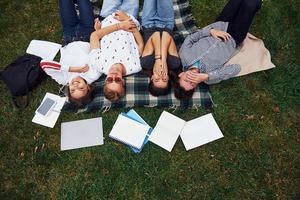 Having good rest. Group of young students in casual clothes on green grass at daytime photo