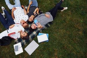 tomando selfie usando un teléfono inteligente. grupo de jóvenes estudiantes con ropa informal sobre hierba verde durante el día foto