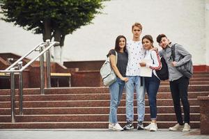 posando para una cámara. grupo de jóvenes estudiantes con ropa informal cerca de la universidad durante el día foto