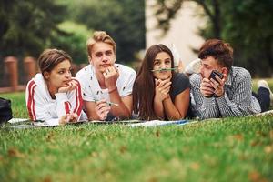 Playful mood. Group of young students in casual clothes on green grass at daytime photo