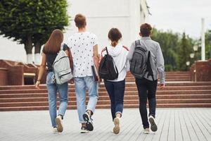 Rear view. Group of young students in casual clothes near university at daytime photo