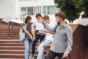 Positive guy. Group of young students in casual clothes near university at daytime photo