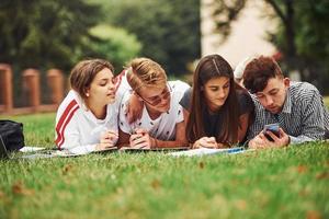 Writing on paper. front view. Group of young students in casual clothes on green grass at daytime photo