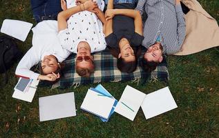 Having good rest. Group of young students in casual clothes on green grass at daytime photo