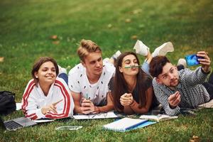 Time for a selfie. Group of young students in casual clothes on green grass at daytime photo