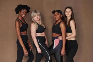 Everyone is beautiful on his own way. Group of multi ethnic women standing in the studio against brown background photo