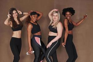 Everyone on his own mood. Group of multi ethnic women standing in the studio against brown background photo