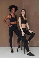 Conception of diversity and beauty. Two multi ethnic female friends stands in the studio with brown background photo