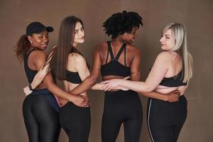 amistad entre jóvenes y adultos. grupo de mujeres multiétnicas de pie en el estudio con fondo marrón foto