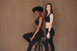 juventud de moda. dos amigas multiétnicas se paran en el estudio con antecedentes marrones foto