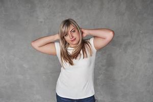 Hands behind the head. Young white woman in the studio standing against grey background photo