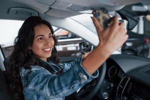 Sharing the happiness. Cute girl with black hair trying her brand new expensive car in the automobile salon photo