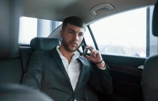 Mature adult. Businessman in official wear have call when sitting on the back of car photo