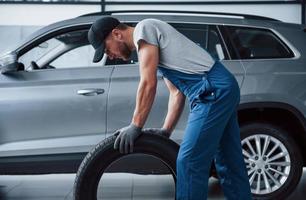 Daily work. Mechanic holding a tire at the repair garage. Replacement of winter and summer tires photo