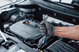 Everything will be fixed. Man's hand in glove holds wrench in front of broken automobile photo