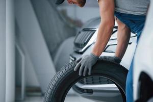 Pushing by the hands. Mechanic holding a tire at the repair garage. Replacement of winter and summer tires photo