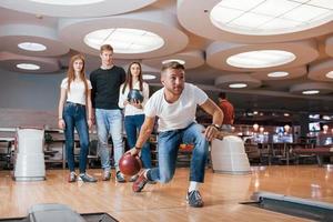 Concentrated at game. Young cheerful friends have fun in bowling club at their weekends photo
