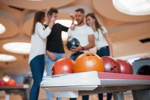 Many different colored balls. Young cheerful friends have fun in bowling club at their weekends photo