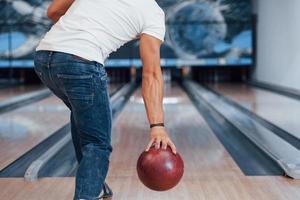 In white shirt and jeans. Rear particle view of man in casual clothes playing bowling in the club photo