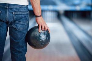 Artificial lighting. Rear particle view of man in casual clothes playing bowling in the club photo