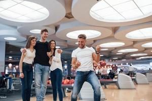 Who is the winner. Young cheerful friends have fun in bowling club at their weekends photo