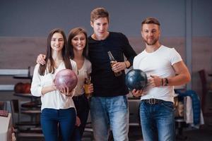 Posing for the camera. Young cheerful friends have fun in bowling club at their weekends photo