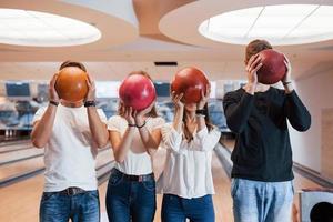 Different colors. Young cheerful friends have fun in bowling club at their weekends photo