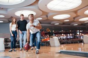 Looking at man throwing the ball. Young cheerful friends have fun in bowling club at their weekends photo