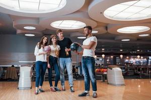 Guy talking about something. Young cheerful friends have fun in bowling club at their weekends photo