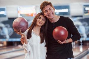 Such a lovely people. Happy couple holding bowling balls in hands and have good time in the club photo