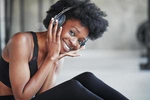 disfrutando de la música. mujer afroamericana con cabello rizado y ropa deportiva tiene un día de fitness en el gimnasio foto