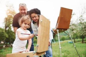 Using red colored brush. Grandmother and grandfather have fun outdoors with granddaughter. Painting conception photo