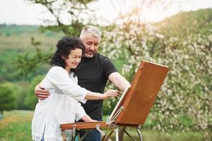 Se ve hermoso. pareja madura tiene días libres y trabaja en la pintura juntos en el parque foto