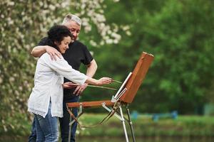 Side view. Mature couple have leisure days and working on the paint together in the park photo