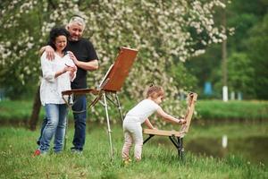 nuevos comienzos. la abuela y el abuelo se divierten al aire libre con su nieta. concepción de la pintura foto